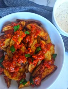 Patatas bravas being served with a drizzle of bravas sauce and a side of garlic aioli.