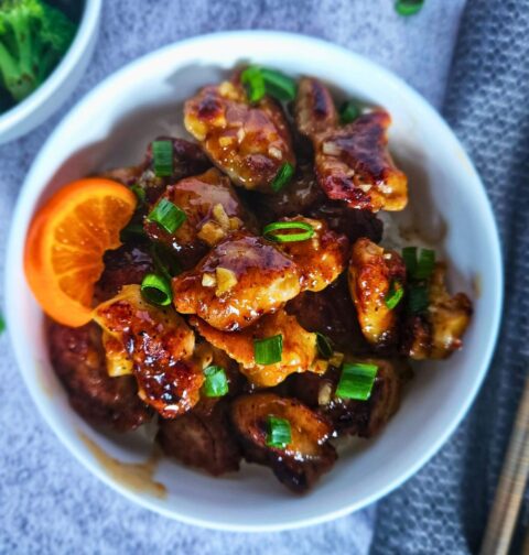Easy orange chicken served over white rice in a bowl alongside chopsticks and a side of broccoli.