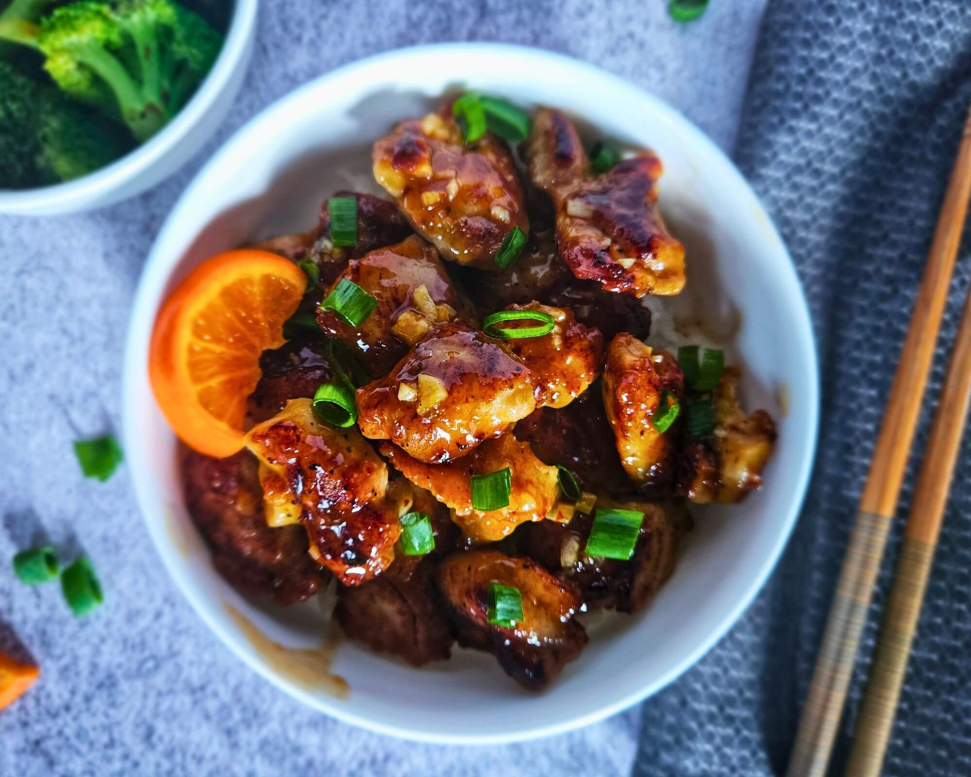 Photo of easy orange chicken being served over rice in a bowl with a side of broccoli. 