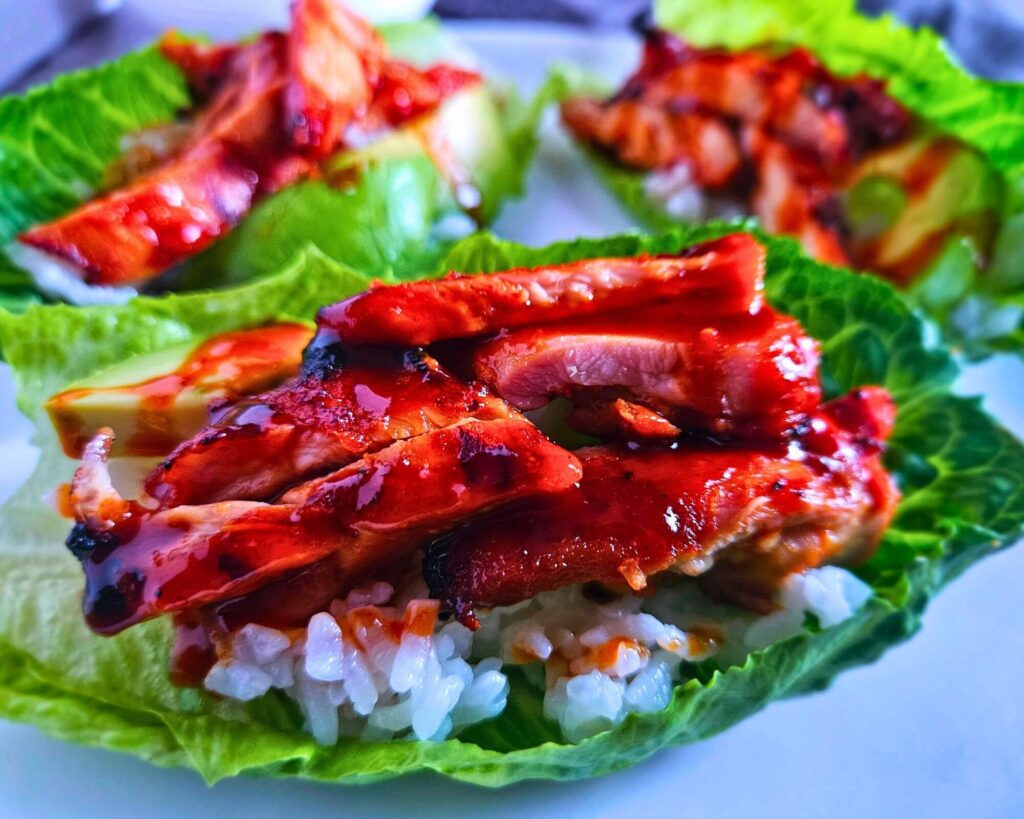 Grilled Korean BBQ chicken thighs in a lettuce wrap layered with white rice, avocado and gochujang drizzle.