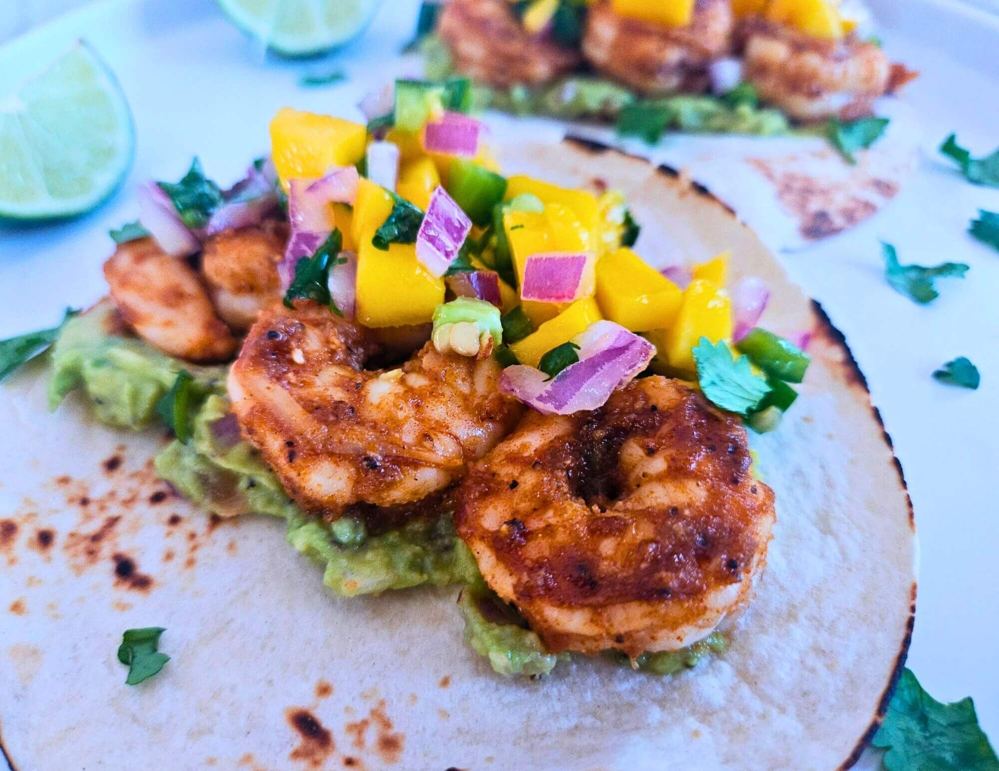 Image of blackened honey lime shrimp tacos with guacamole and mango salsa. 