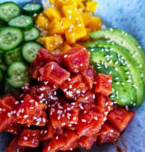 Spicy tuna poke bowl with spicy tuna over rice with sliced avocado, cucumbers and mango.