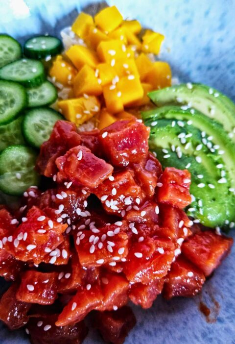 Spicy tuna poke bowl with spicy tuna over rice with sliced avocado, cucumbers and mango.