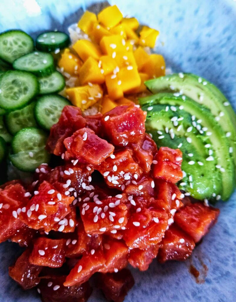 Spicy tuna poke bowl with spicy tuna over rice with sliced avocado, cucumbers and mango.