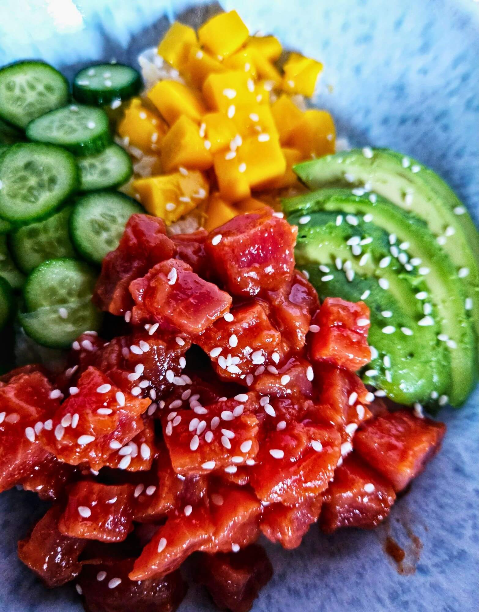 Spicy tuna poke bowl with spicy tuna over rice with sliced avocado, cucumbers and mango.