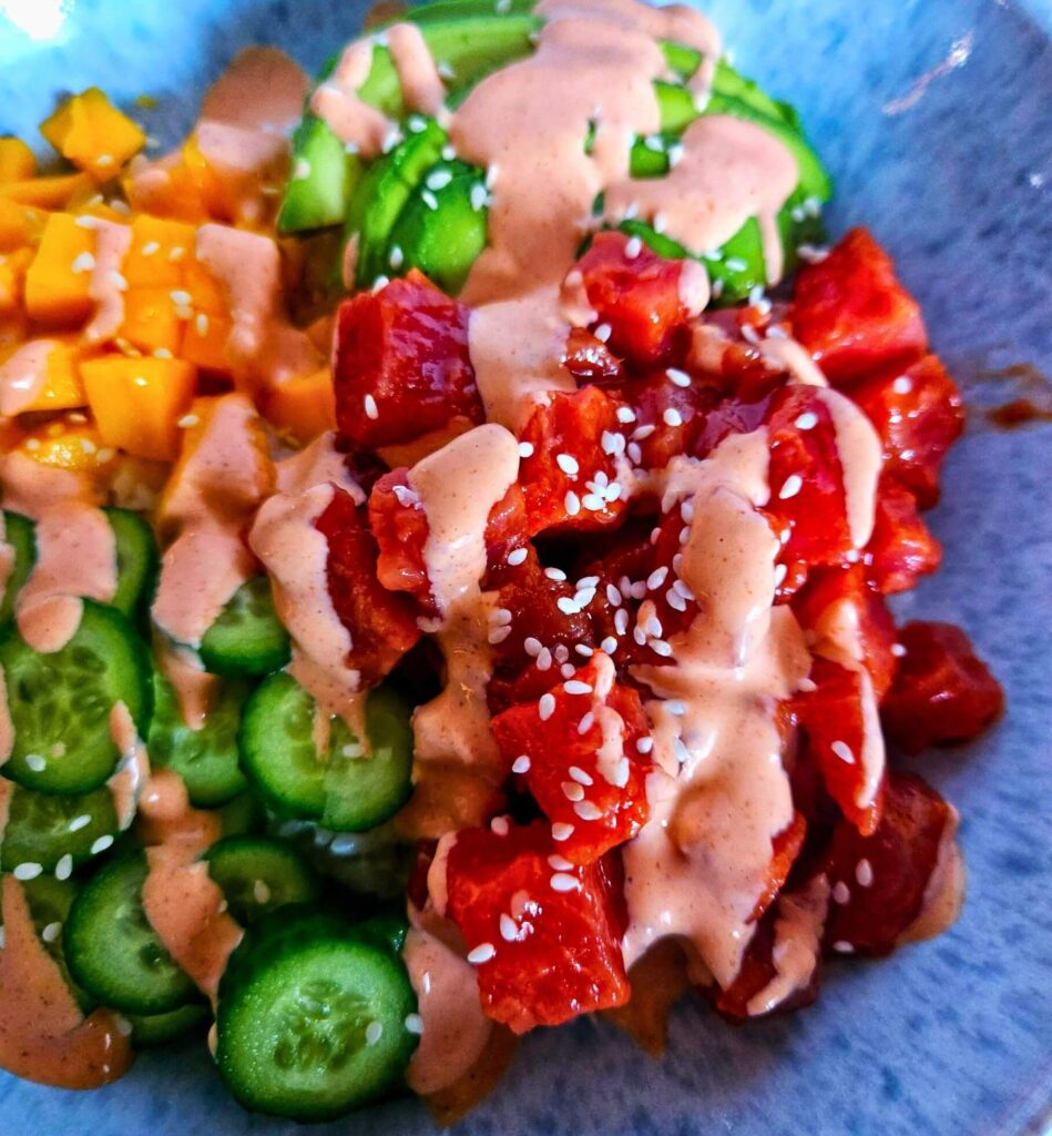 Spicy tuna poke bowl with spicy tuna over rice with sliced avocado, cucumbers and mango with spicy mayo drizzle.