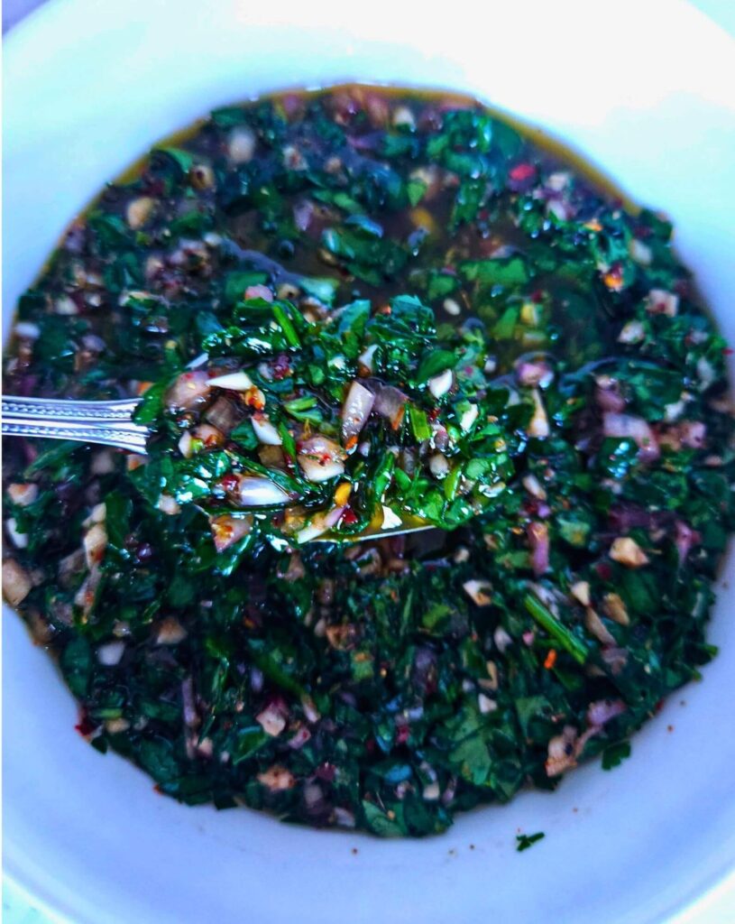 chimichuri sauce 4 Close up image of chimichurri sauce in a bowl being scooped with a spoon.