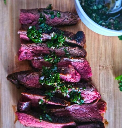 Marinated flank steak sliced again the grain on a cutting board with a drizzle of chimichurri.