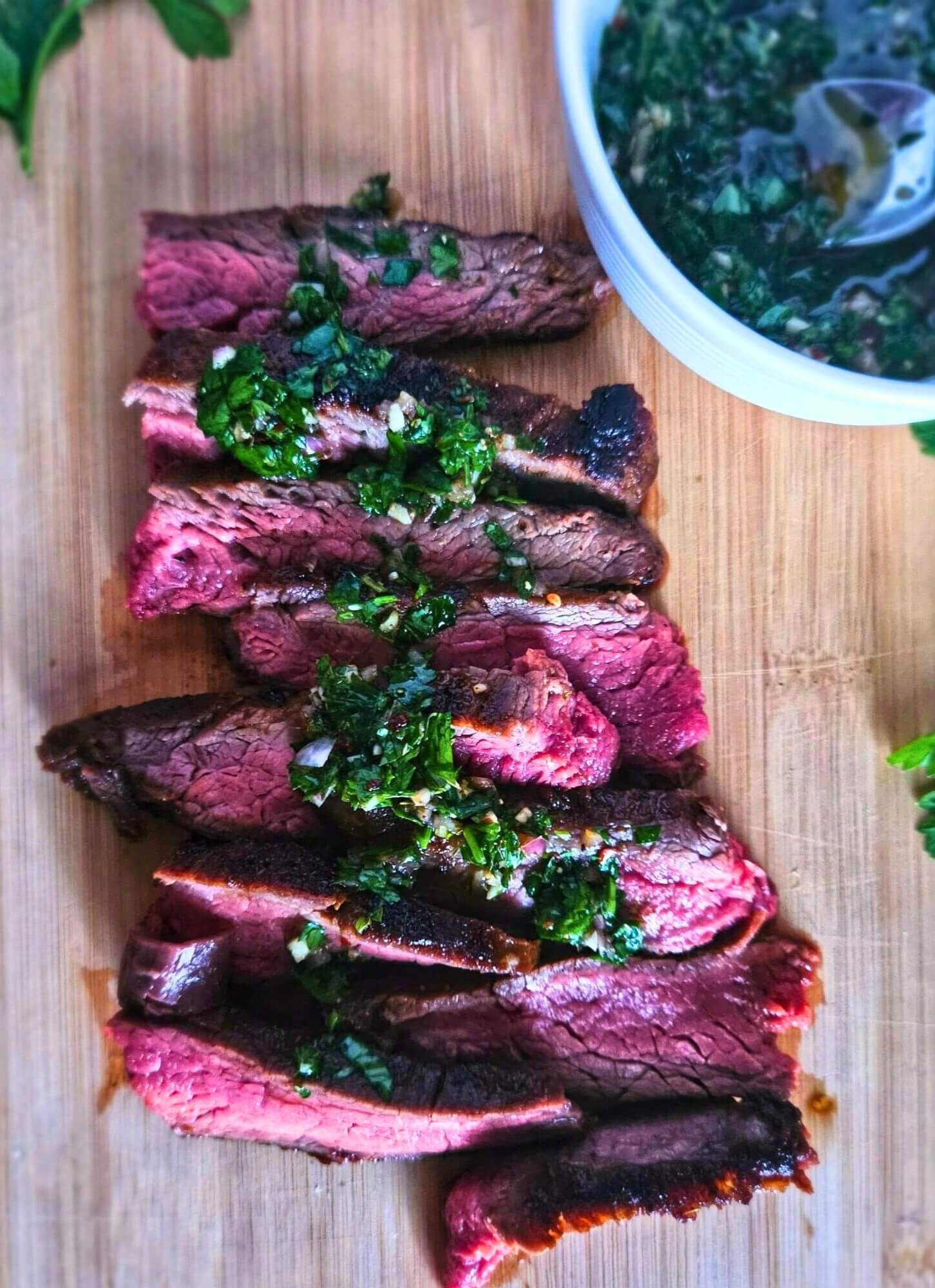 Marinated flank steak sliced against the grain on a cutting board with a drizzle of chimichurri.