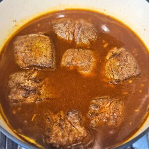 Image of chuck roast being braised in dutch oven.