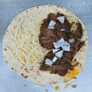 Image of barbacoa taco being built with beef, cheese and onions.