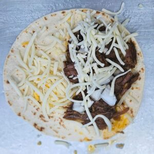 Image of barbacoa tacos being built with cheese and beef.