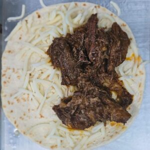 Image of barbacoa taco being built with beef and cheese.