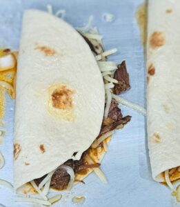 Image of barbacoa taco being folded and ready to bake in the oven. 