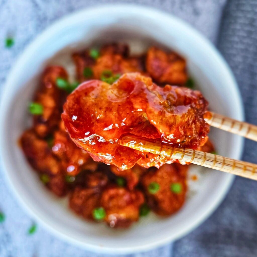 Image of air fryer Korean fried chicken being picked up with chopsticks. 