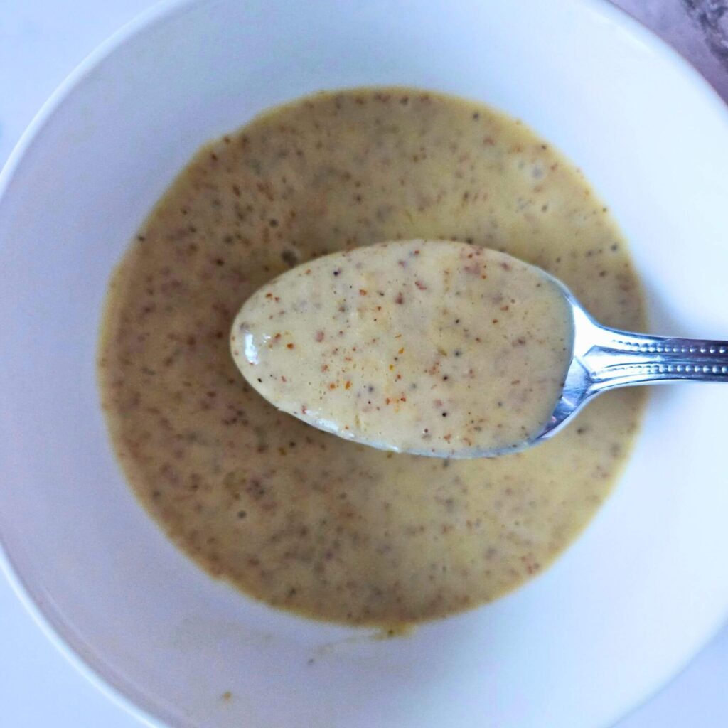 Lemon Dijon dressing being scooped with a spoon.
