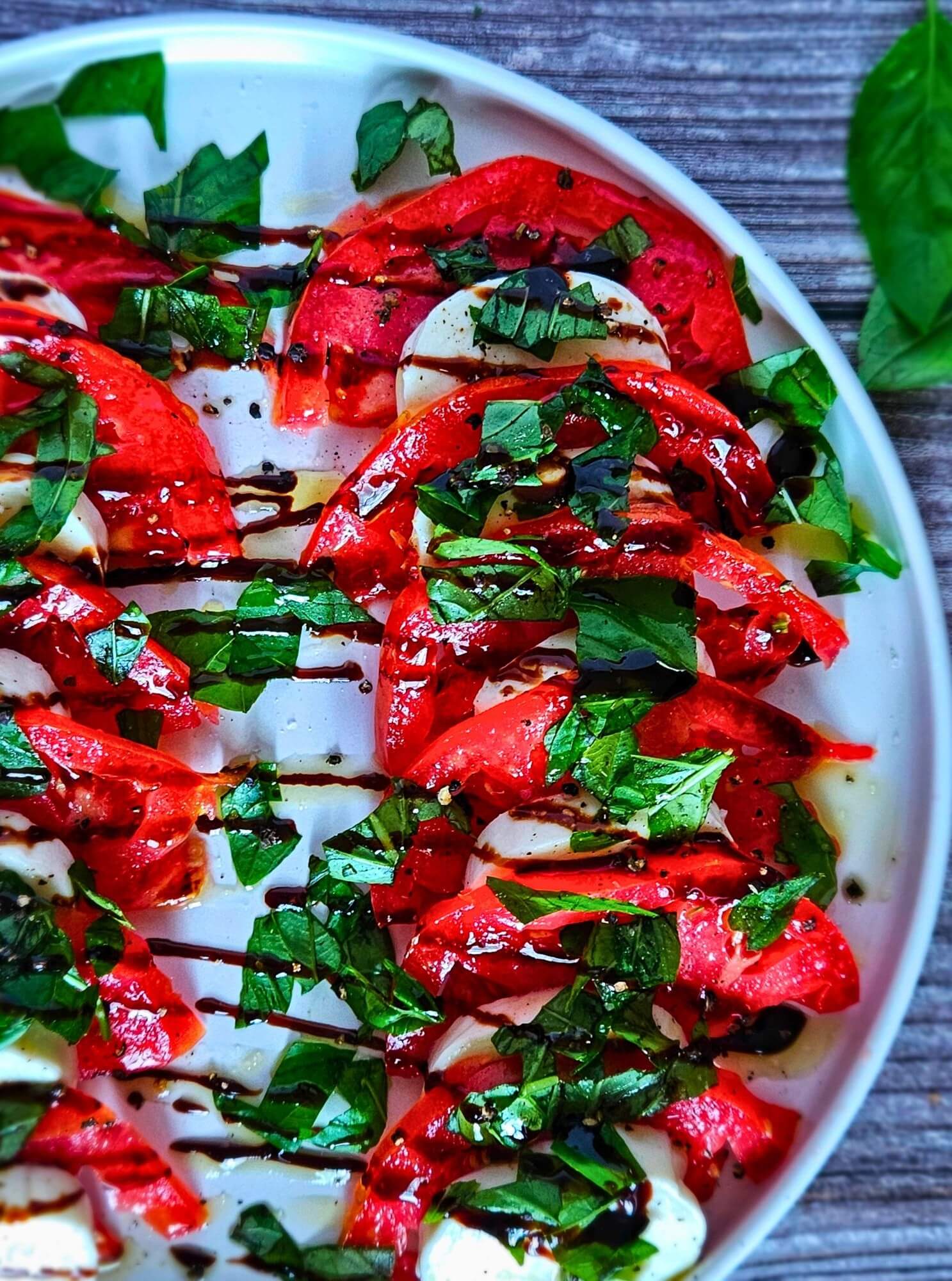 Image of caprese salad with sliced tomatoes, fresh mozzarella, chopped basil and balsamic drizzle.