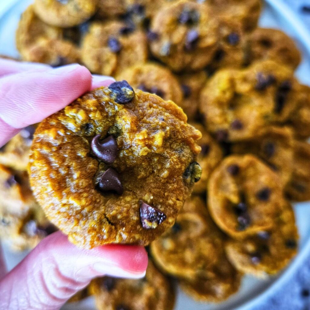 Close up image of gluten free pumpkin muffins being held over a plate a mini pumpkin muffins.
