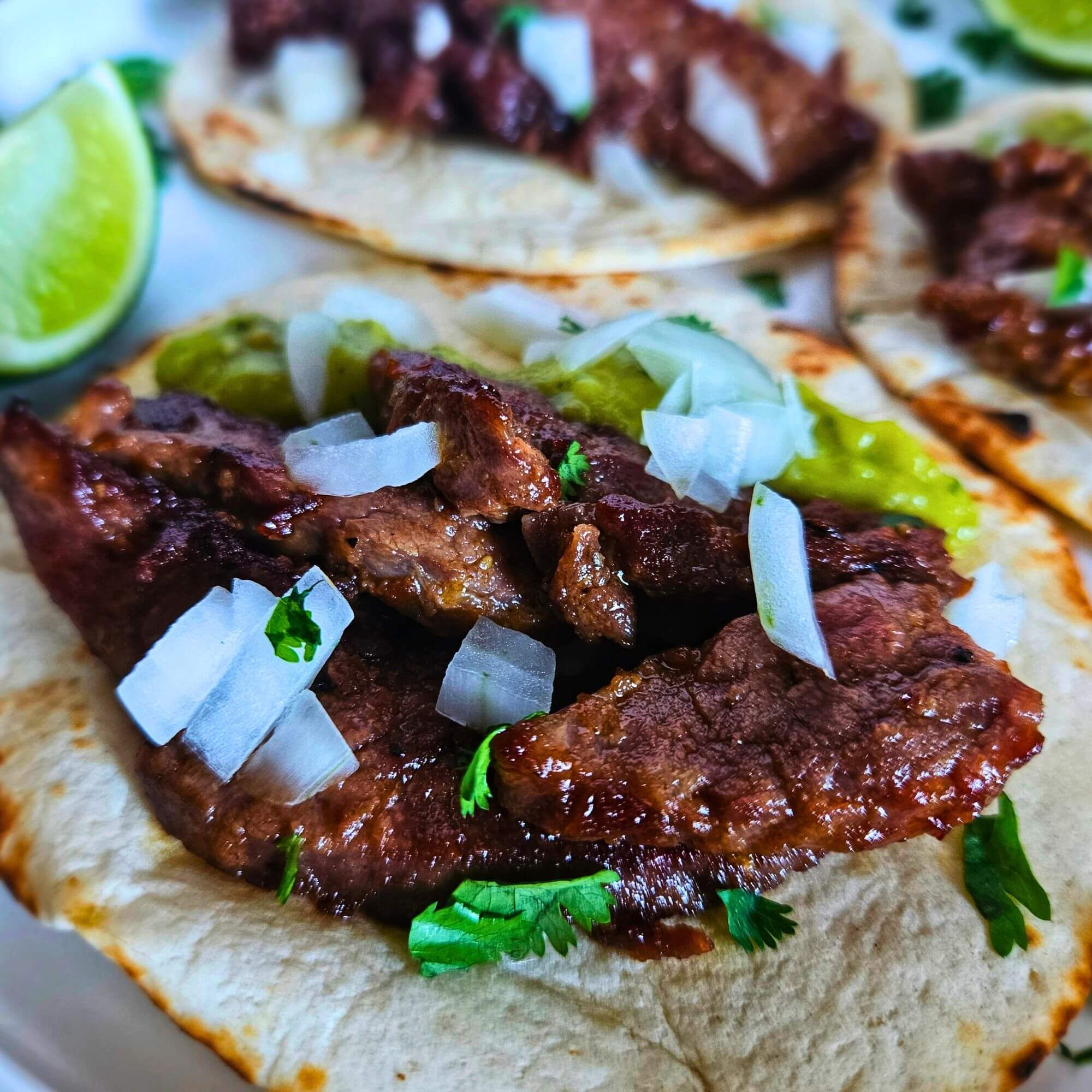 Close up image of steak tacos topped with avocado tomatillo salsa and chopped white onion.