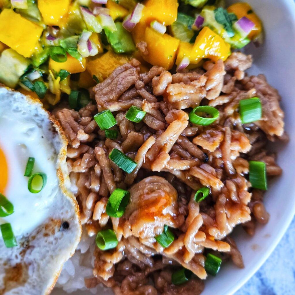 teriyaki chicken bowl 10 Close up image of teriyaki chicken rice bowl with avocado mango salsa over white rice and a fried egg.