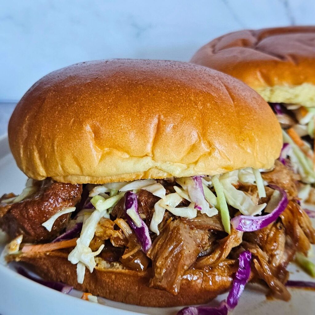 Image of Dutch oven pulled pork braised in apple cider made into a pulled pork sandwich with creamy coleslaw.