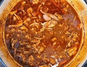 Shredded pulled pork returned to the Dutch oven with braising liquid and BBQ sauce.