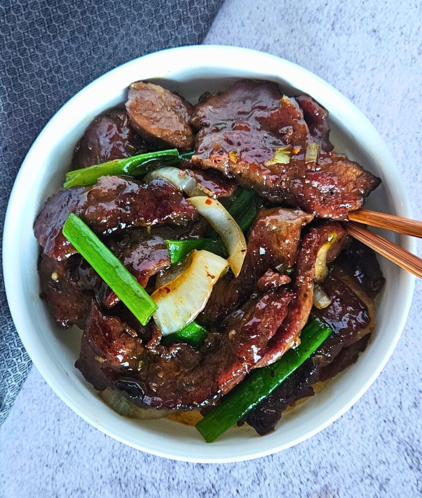 Mongolian beef stir fry being served over white rice with chopsticks.