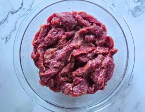 Flank steak slices into strips and marinated in a bowl before searing.