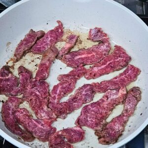 Flank steak being seared in a skillet for the Mongolian beef stir fry recipe.