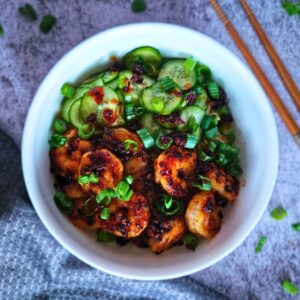Image of peanut noodles with chili shrimp and pickled cucumbers and green onions in a bowl before eating. 
