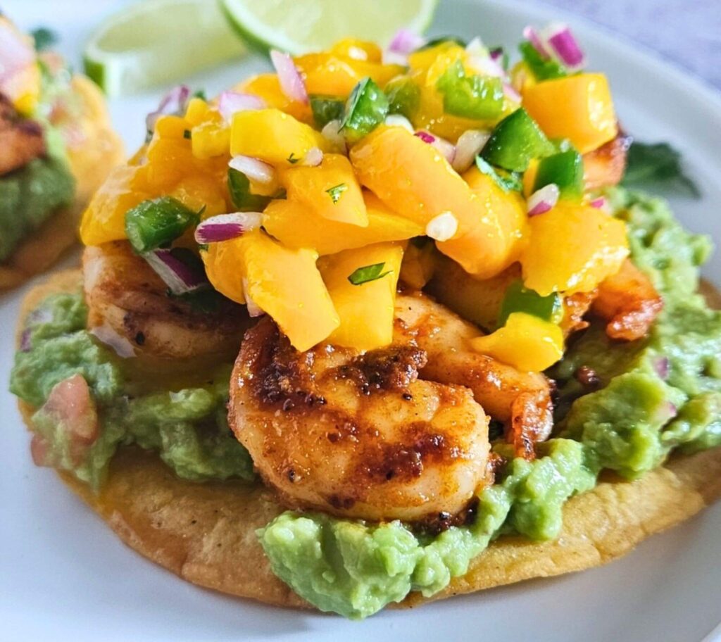 Close up image of shrimp tostadas with guacamole, blackened shrimp and mango salsa layered on a homemade tostada.