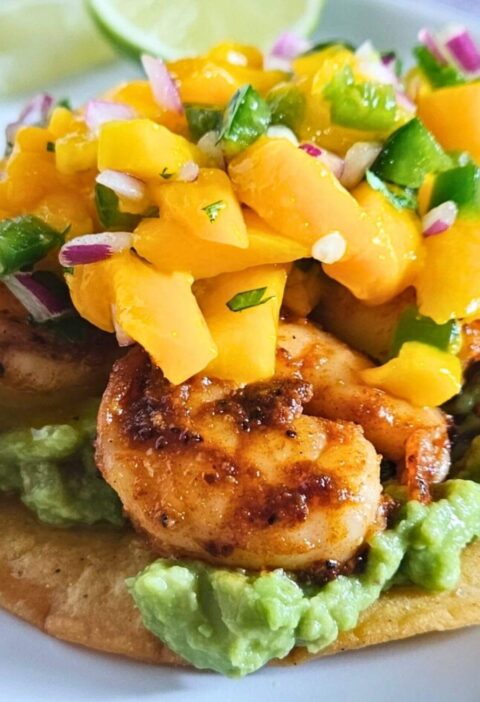 Close up image of shrimp tostadas with guacamole, blackened shrimp and mango salsa layered on a homemade tostada.