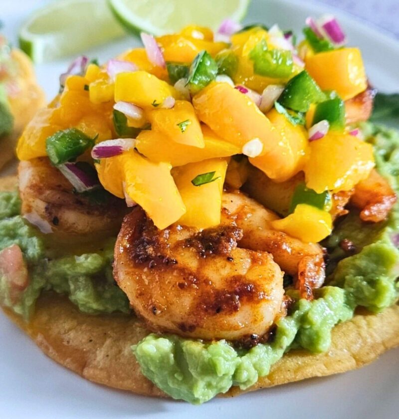 Close up image of shrimp tostadas with guacamole, blackened shrimp and mango salsa layered on a homemade tostada.