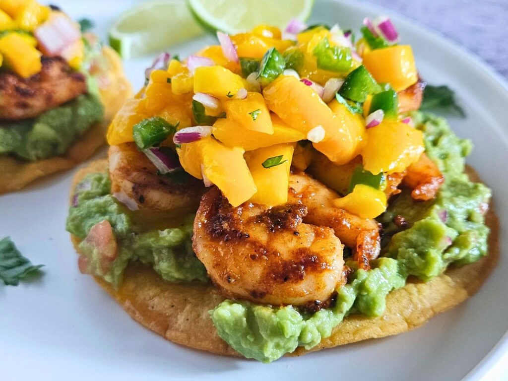 Image of shrimp tostadas with guacamole, blackened shrimp and mango salsa layered on a homemade tostada.