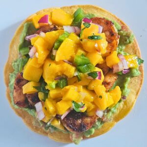 Shrimp tostada after being assembled with the homemade tostada, guacamole, blackened shrimp and mango salsa.