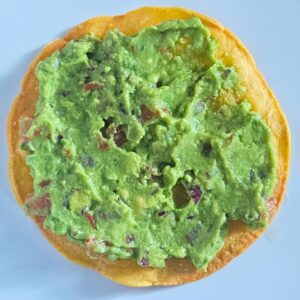 Shrimp tostada being assemble with homemade tostada and guacamole.
