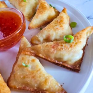 Homemade crab rangoons being served on a plate with sweet chili sauce.