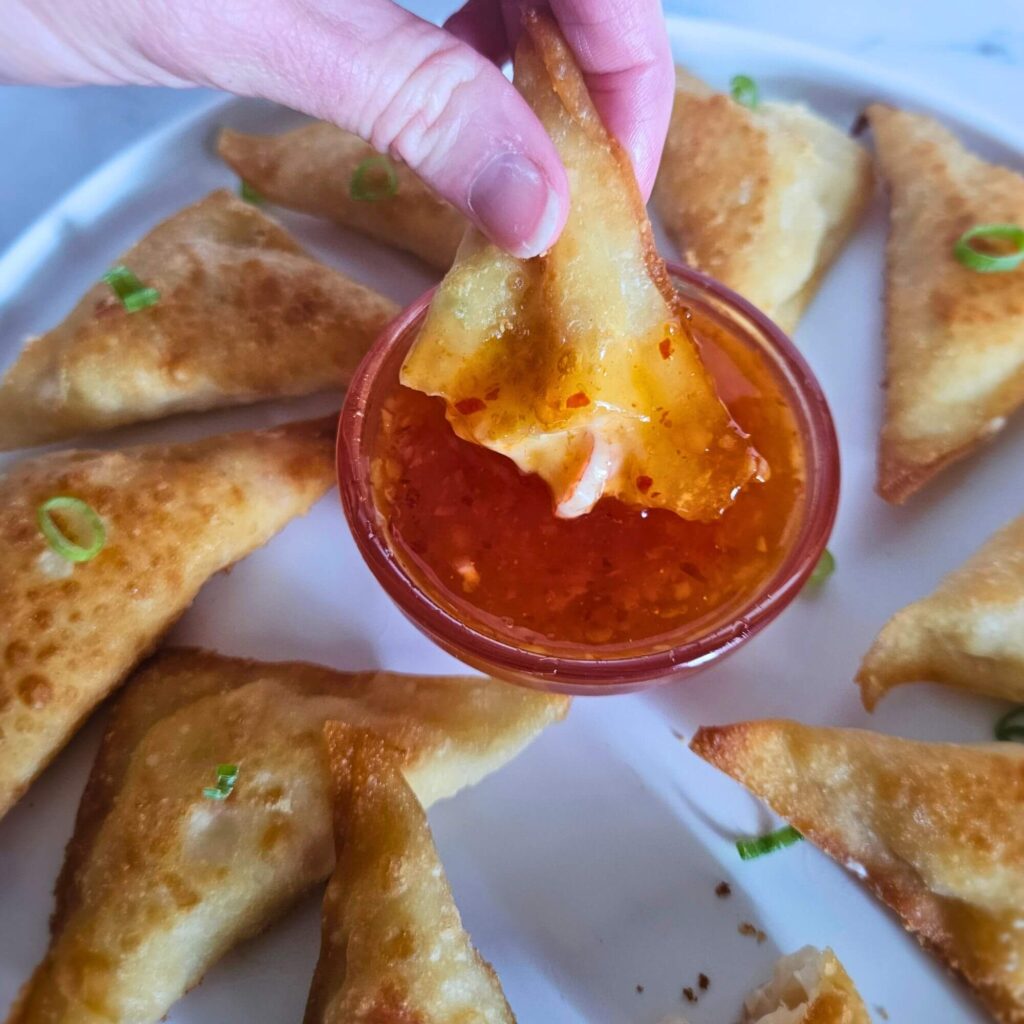 Homemade crab rangoons being dipped in sweet chili sauce.