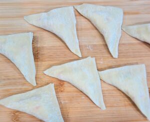 Step-by-step photo of how to fold crab rangoons with cream cheese and crab filling.
