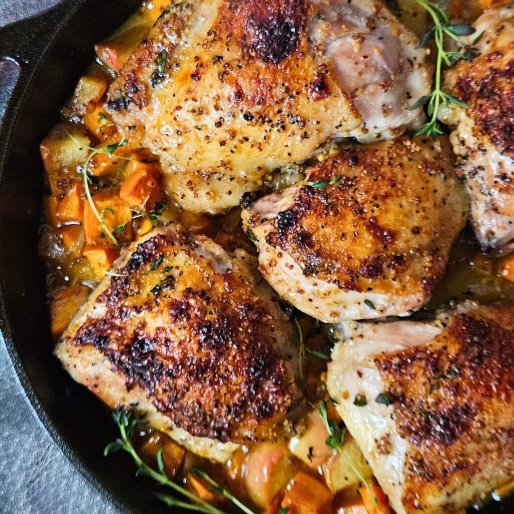 Apple Cider Chicken 16 Apple Cider Glazed Chicken Thighs with sweet potatoes in a cast iron skillet after roasting.