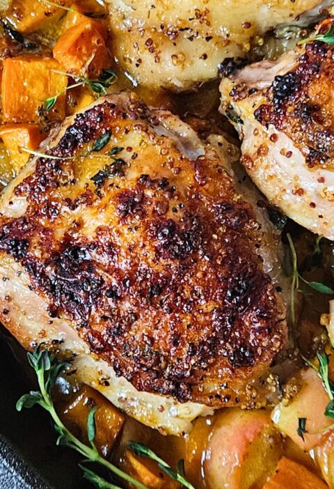 Close up image of apple cider glazed chicken thighs over roasted sweet potatoes and apples.