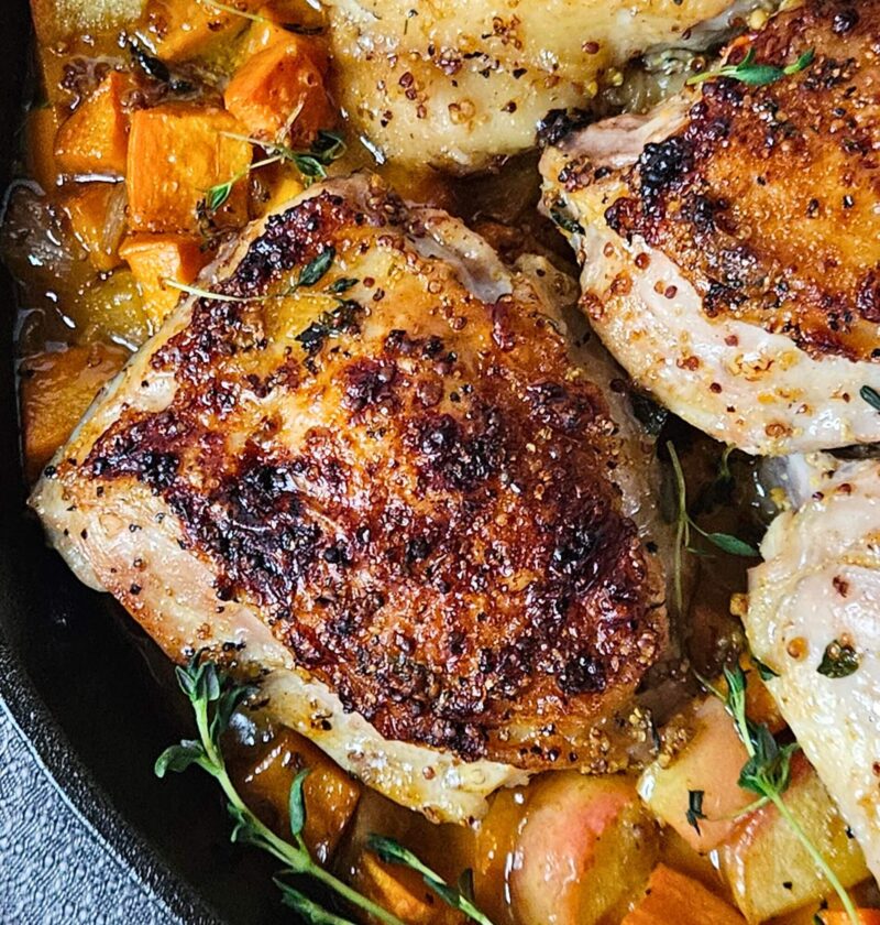 Close up image of apple cider glazed chicken thighs over roasted sweet potatoes and apples.