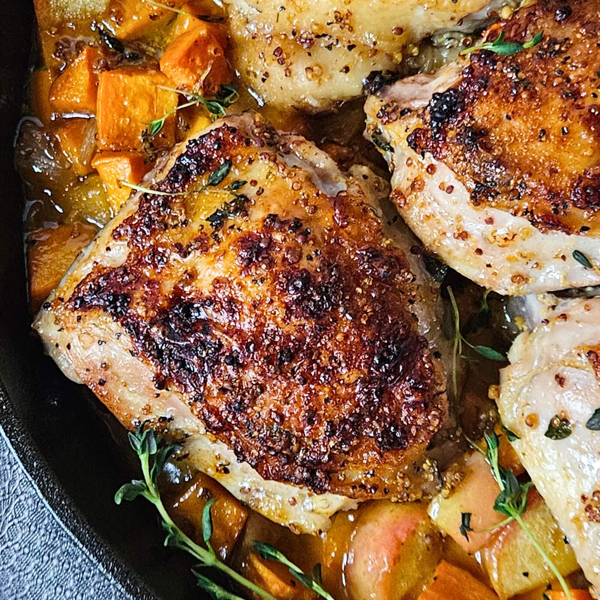 Close up image of apple cider glazed chicken thighs with sweet potatoes and apples in a cast iron.