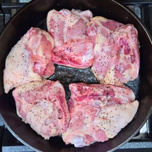 Chicken thighs searing skin side down in cast iron skillet.
