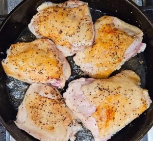 Chicken thighs searing skin side up in cast iron skillet.