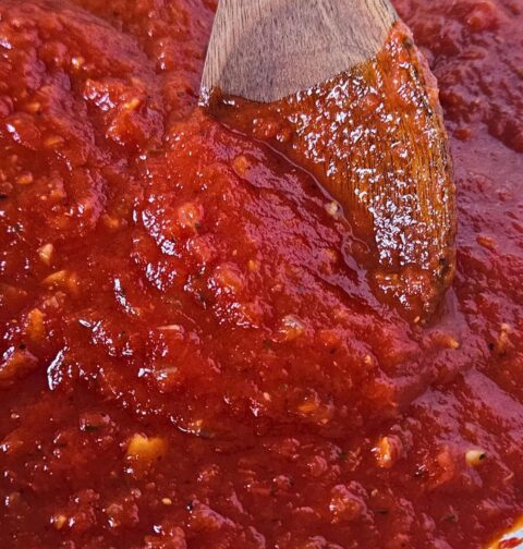 Close up image of easy marinara sauce being stirred by wooden spoon.