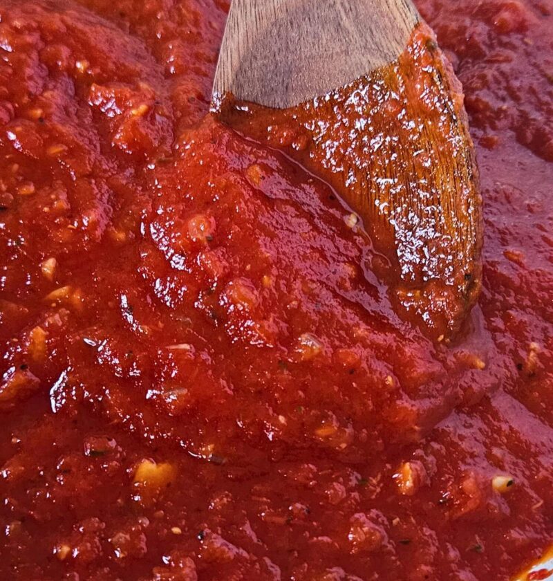 Close up image of easy marinara sauce being stirred by wooden spoon.