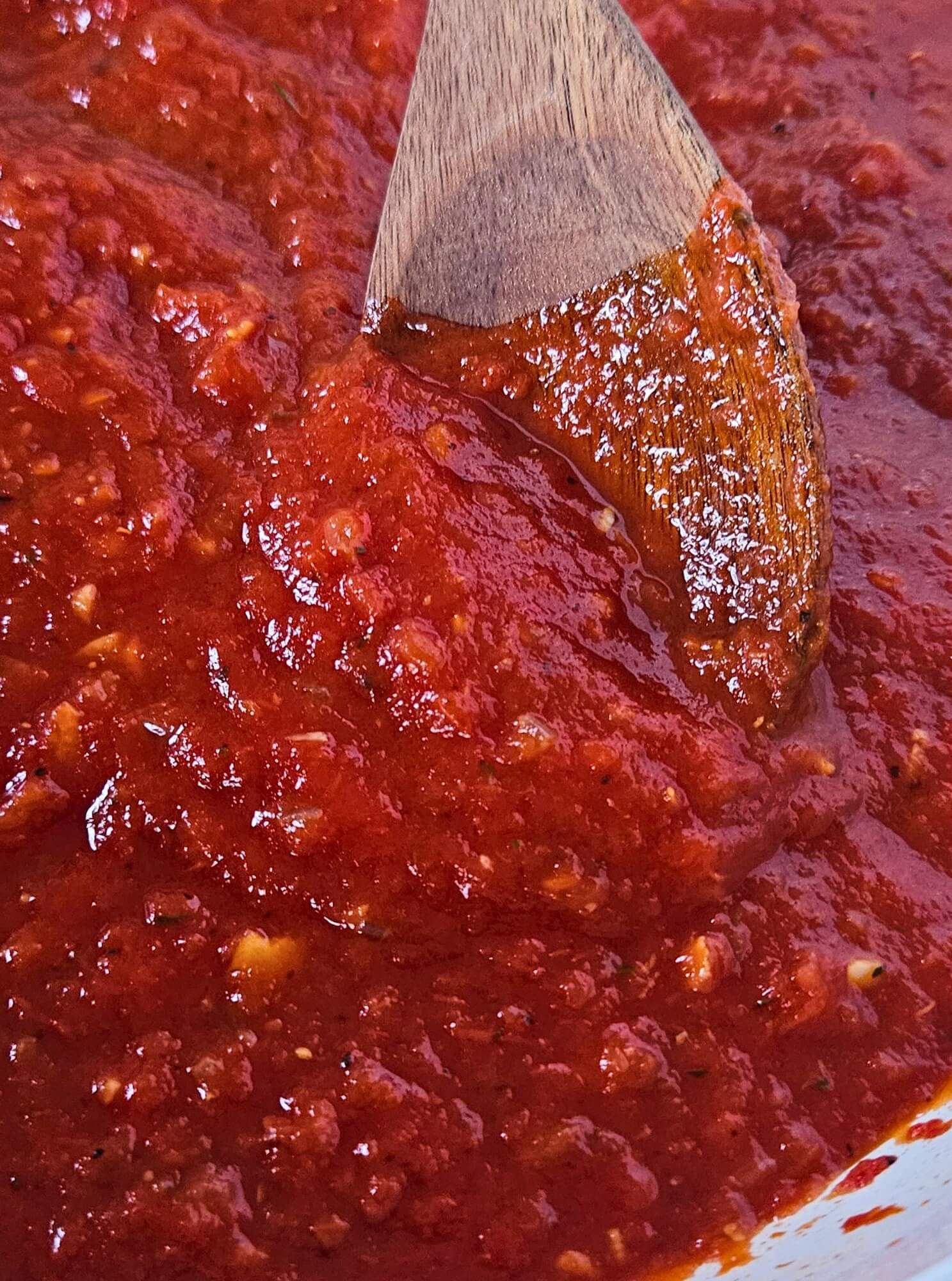Close up image of easy marinara sauce being stirred by wooden spoon after simmering.
