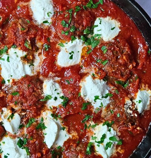 Ricotta meatballs in homemade marinara sauce in a cast iron skillet with dollops or ricotta cheese on top.