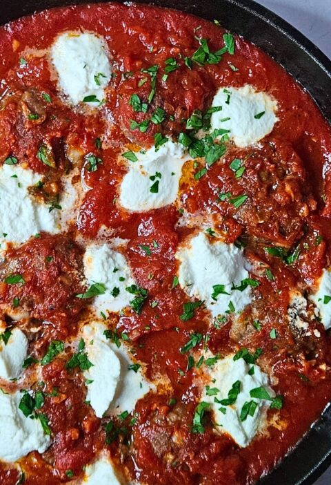 Ricotta meatballs in homemade marinara sauce in a cast iron skillet with dollops or ricotta cheese on top.